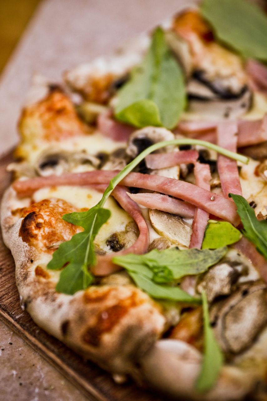 Pizza with ham and rocket and mushrooms on a wooden table.