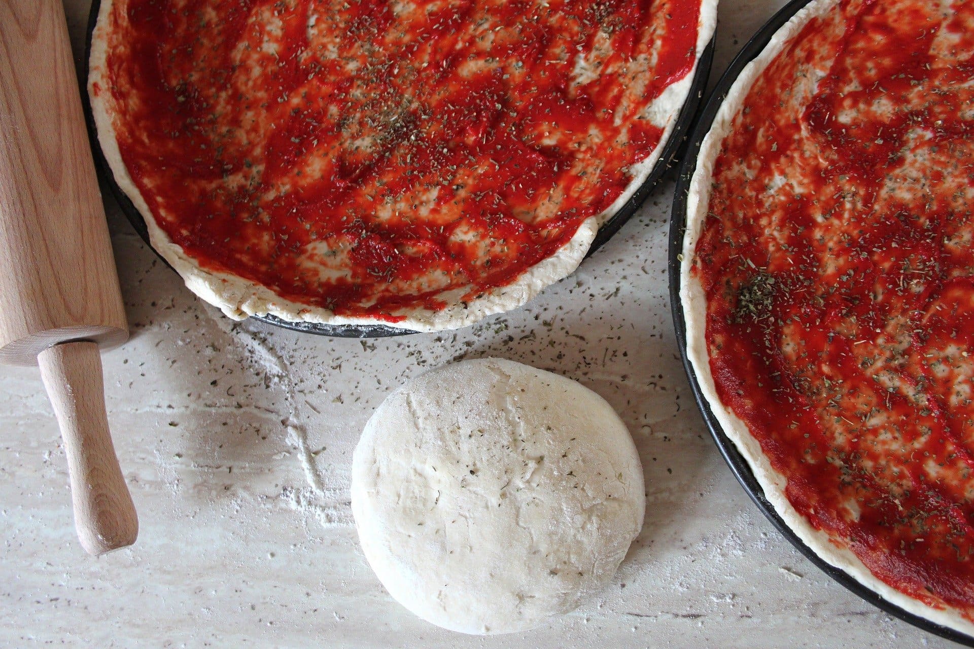 Pizza bases with tomato paste and spices beside a lump of fresh pizza dough.
